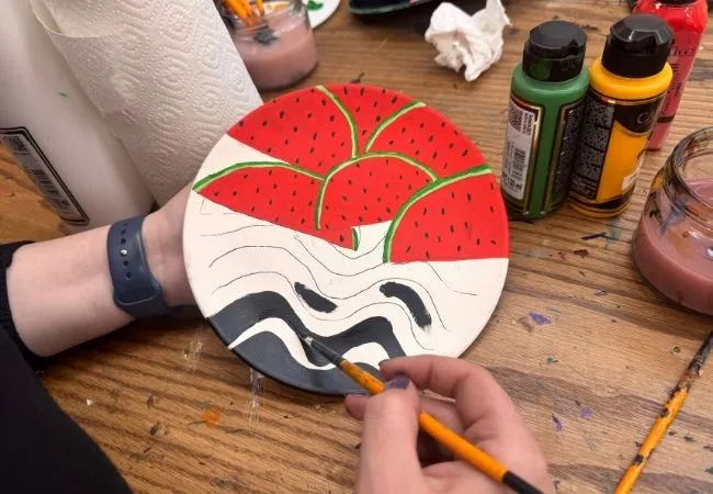 Participant painting a watermelon design on a ceramic plate