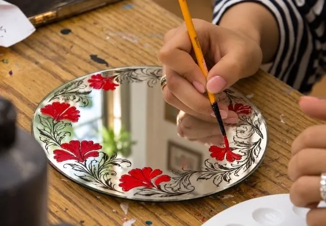 Participant painting red floral patterns on a decorative mirror